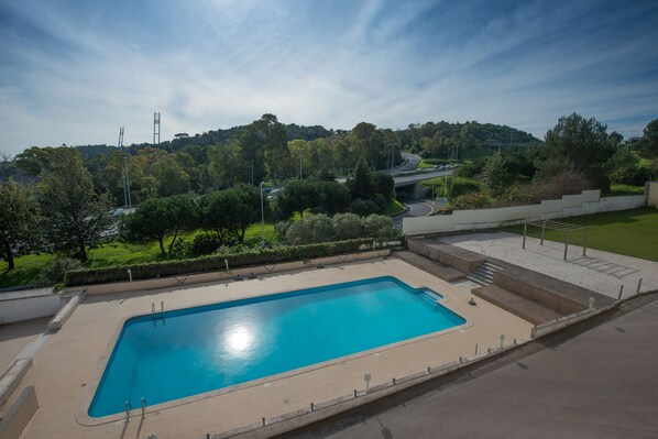 A rectangular swimming pool with a clear blue water surface, surrounded by a concrete deck and a low stone wall. - Amazonia Jamor Hotel (Oeiras)