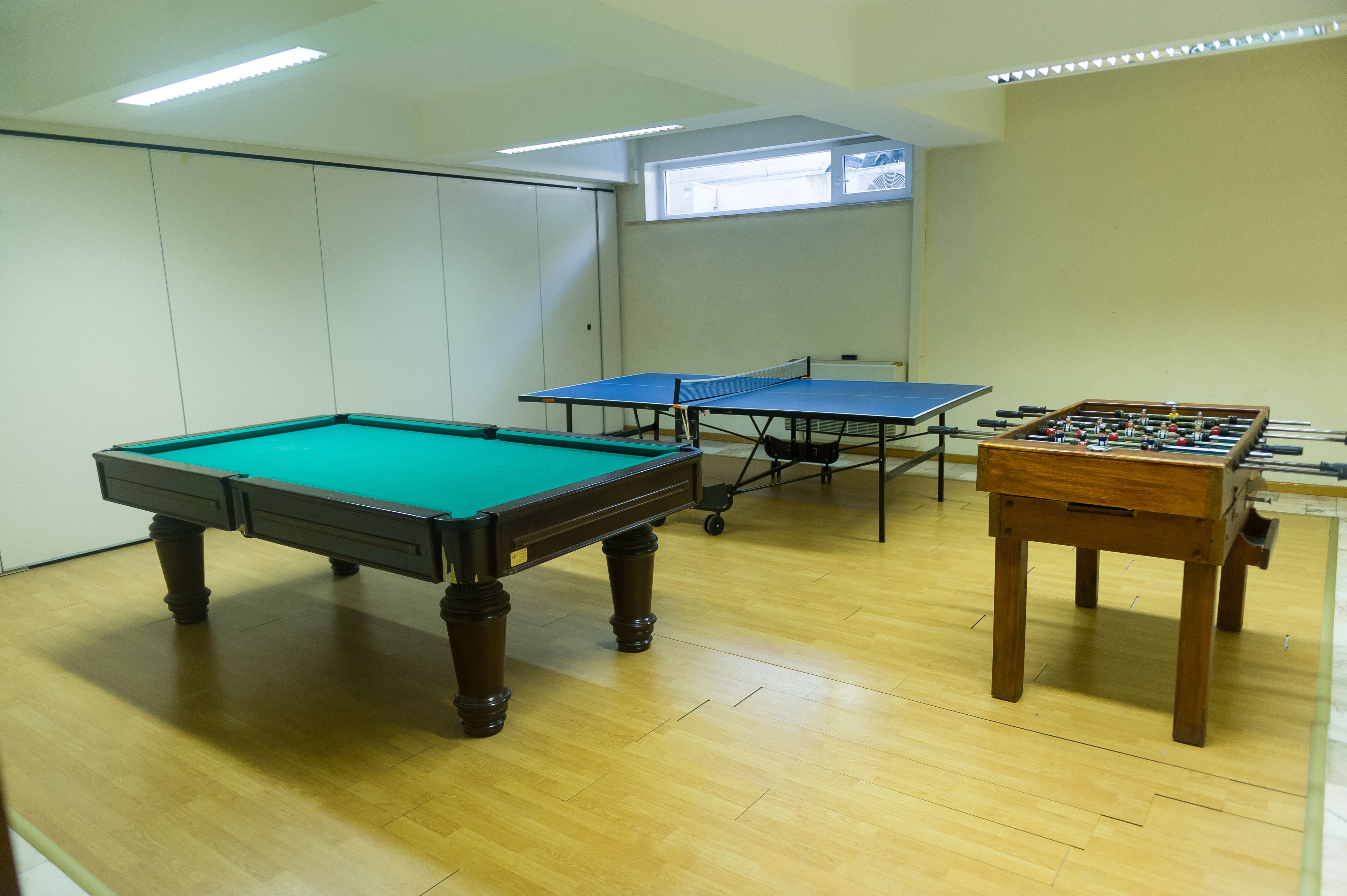 A room with a pool table, two ping pong tables, and a foosball table.