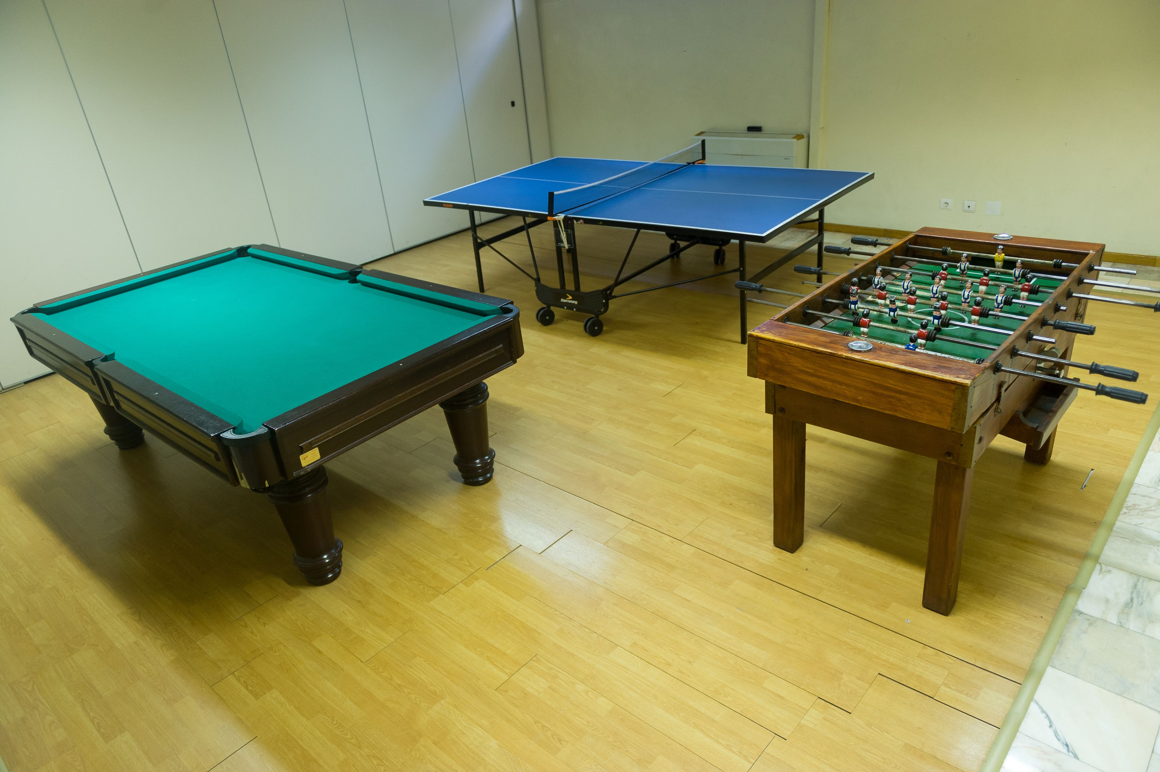 A pool table, two foosball tables, and a ping pong table in a room with wooden flooring.