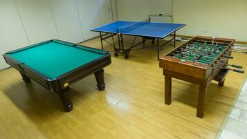 A pool table, two foosball tables, and a ping pong table in a room with wooden flooring.