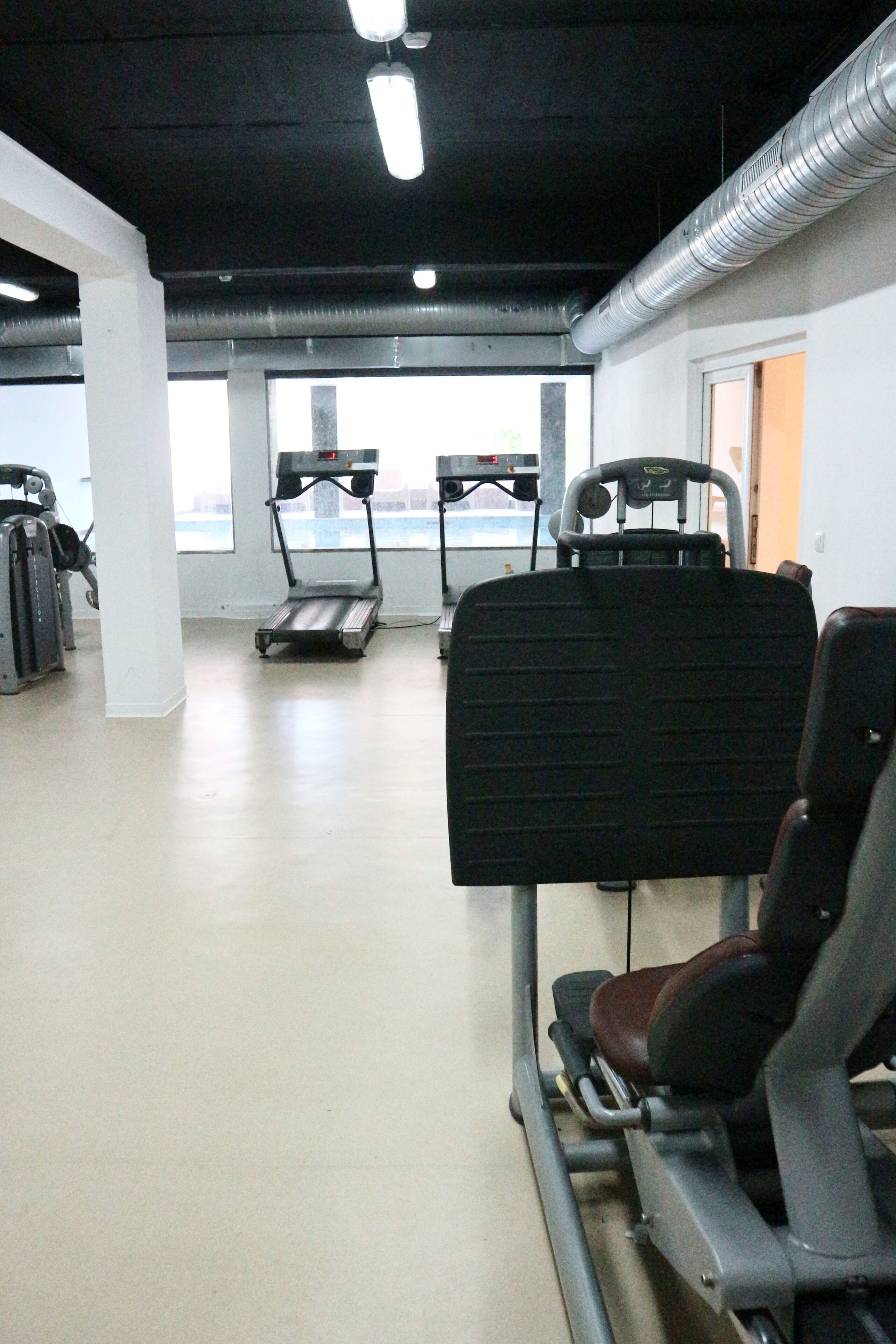 A gym with treadmills, weight machines, and a large window.
