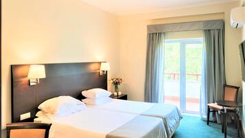 A hotel room with two beds, a desk, a chair, a TV, and a balcony with curtains.