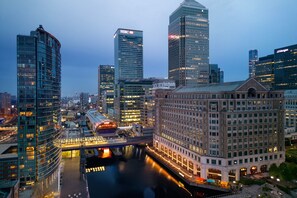 A cityscape with modern high-rise buildings, including a prominent HSBC building, a historic building with arched windows, and a river running through the city. - Marriott Executive Apartments London, Canary Wharf (London)
