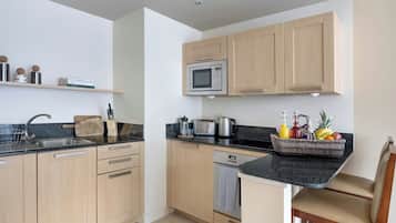 A modern kitchen with wooden cabinets, a microwave, a toaster, and a coffee maker. There is a sink, a dish rack, and a fruit basket on the counter.