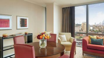 Habitación de hotel con una mesa redonda de comedor, dos sillas, un sofá y un amplio ventanal con vistas a la ciudad.