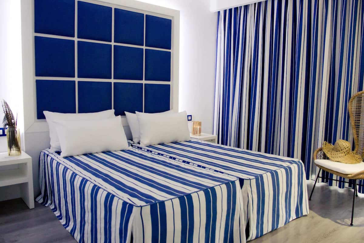 A bedroom with a large bed, a nightstand, a wicker chair, and a striped curtain.