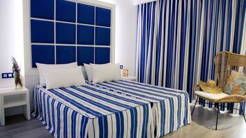 Un dormitorio con una cama grande, una mesita de noche, una silla de mimbre y una cortina a rayas.