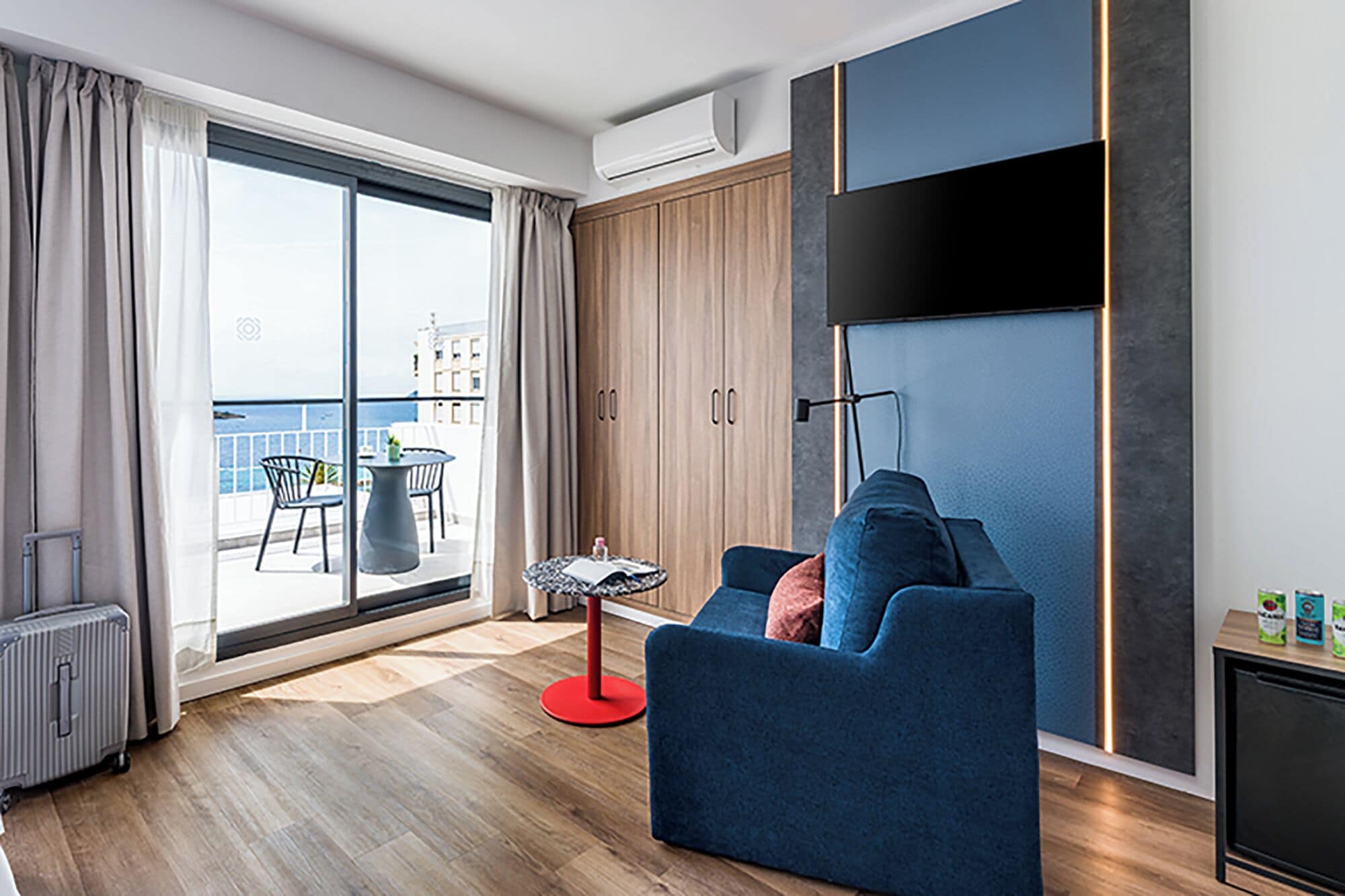 Ein modernes Wohnzimmer mit einer Couch, einem kleinen Tisch, einem Koffer und Blick ins Freie.