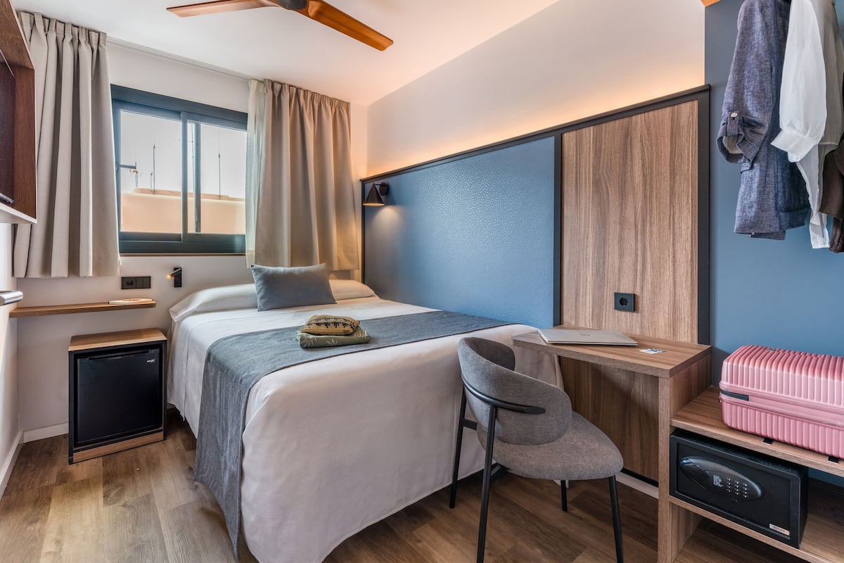 Camera d'albergo compatta con un letto, una scrivania, una sedia e una valigia.