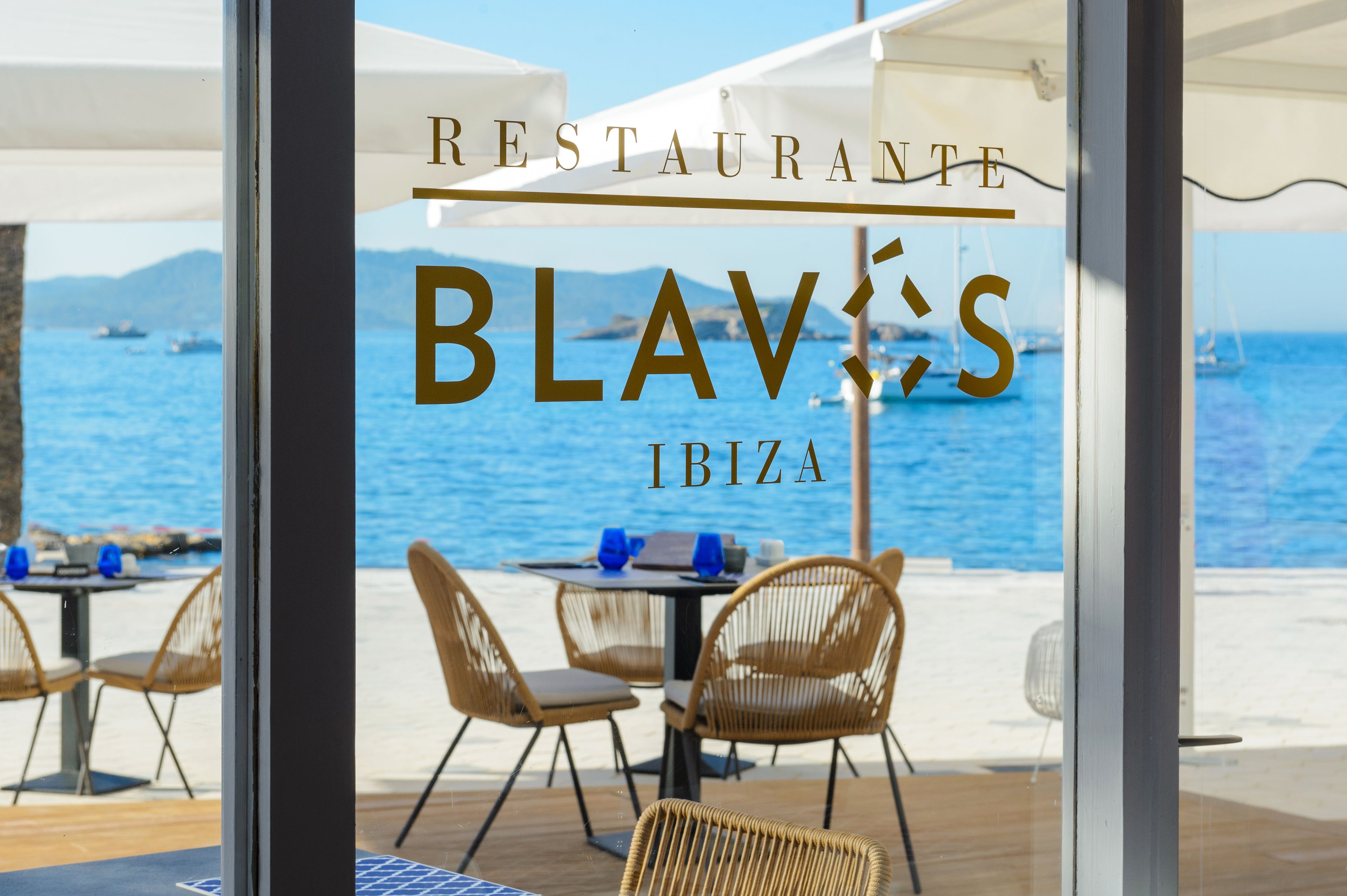 A restaurant with outdoor seating overlooking the sea, featuring a clear view of boats and the coastline.