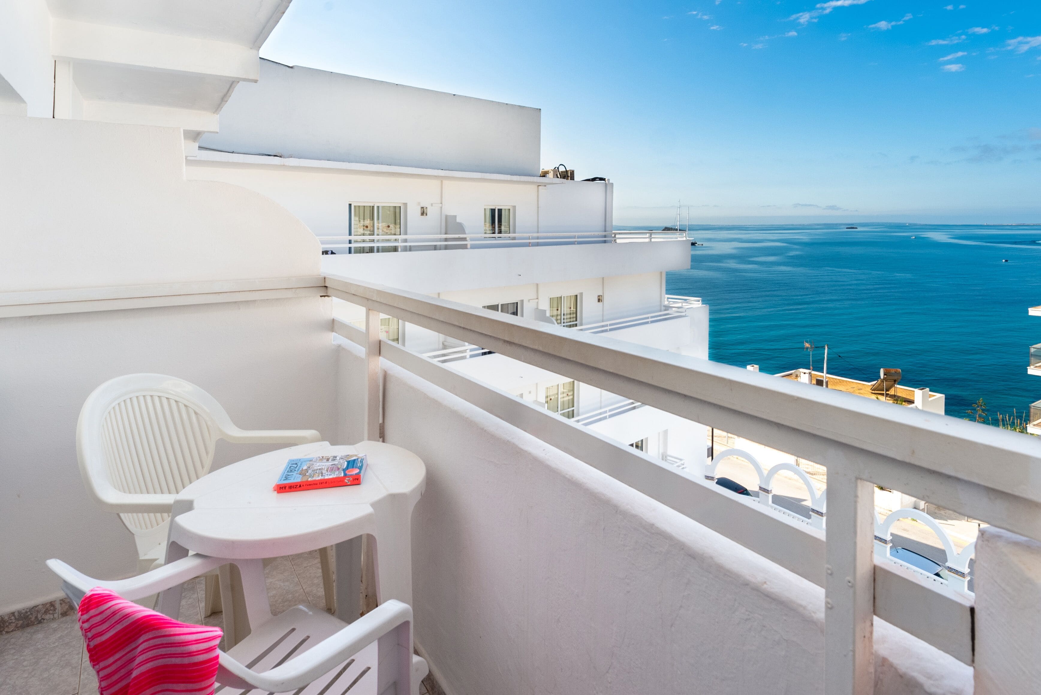 A balcony with a white table, chairs, and a view of the sea.