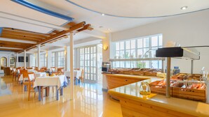 Un vaste espace dédié à la salle à manger, avec des tables et des chaises en bois, un buffet proposant divers plats, et de grandes fenêtres laissant entrer la lumière naturelle.