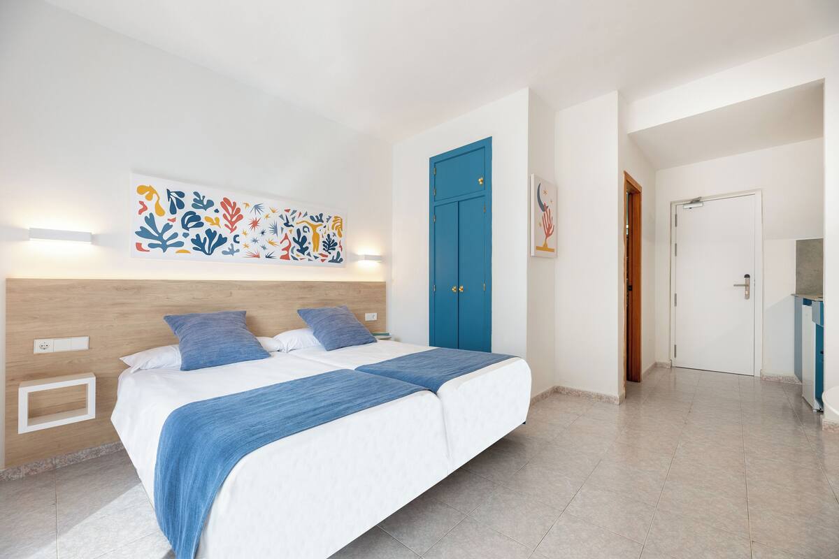 Une chambre à coucher avec un lit, une porte bleue et une œuvre d’art accrochée au mur.