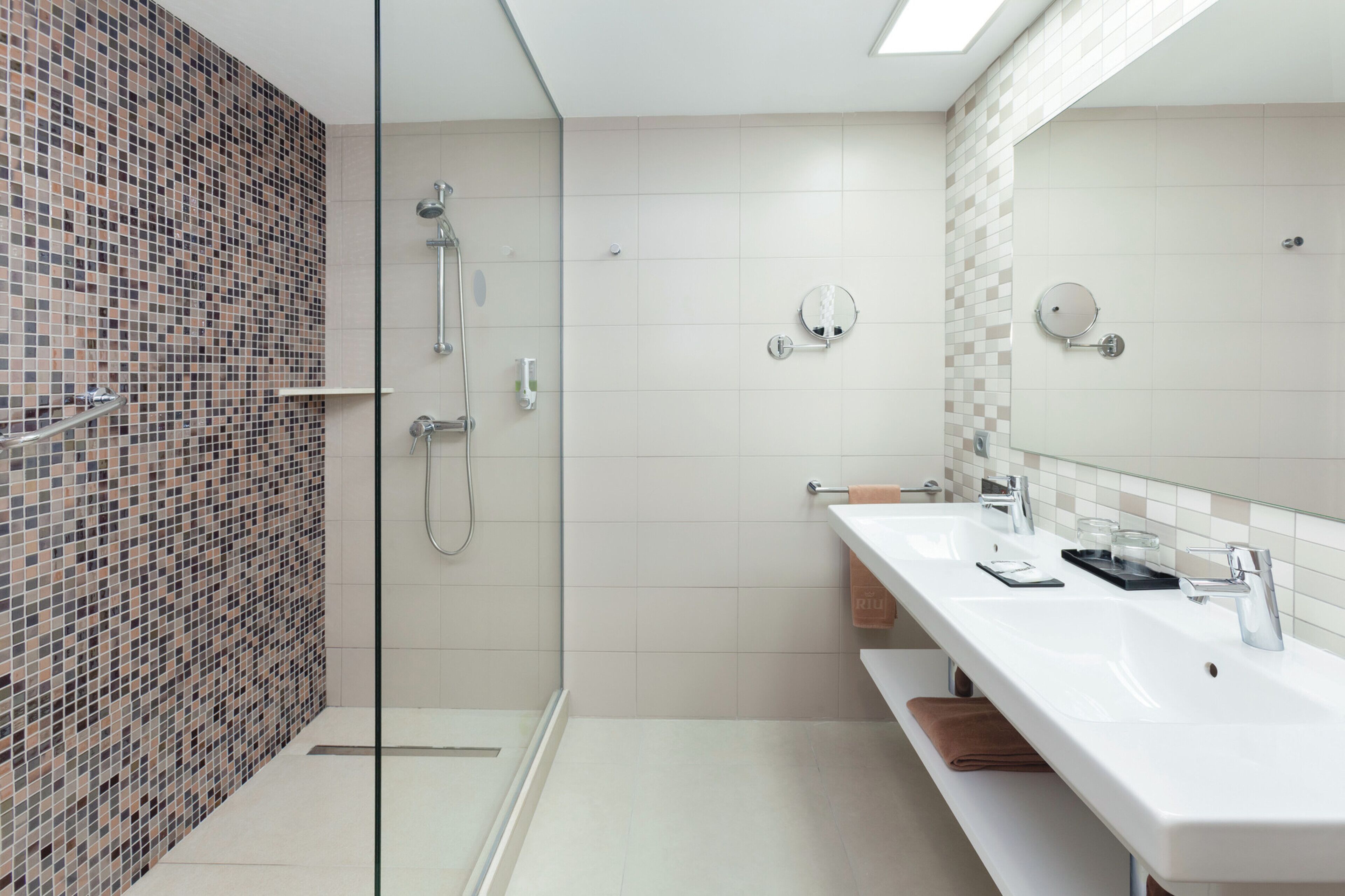 Un baño moderno con cabina de ducha de vidrio, dos lavamanos y un espejo grande.