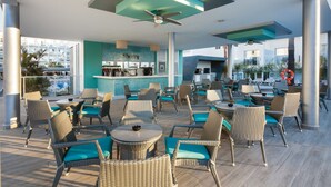 An outdoor dining area with wicker chairs and tables, a bar area with a 'Cherry' sign, and large windows offering views of the city. - Hotel Riu Costa del Sol - All Inclusive (Torremolinos)