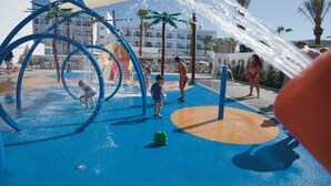 A water play area with blue and orange flooring, water jets, and palm trees in the background. - Hotel Riu Costa del Sol - All Inclusive (Torremolinos)