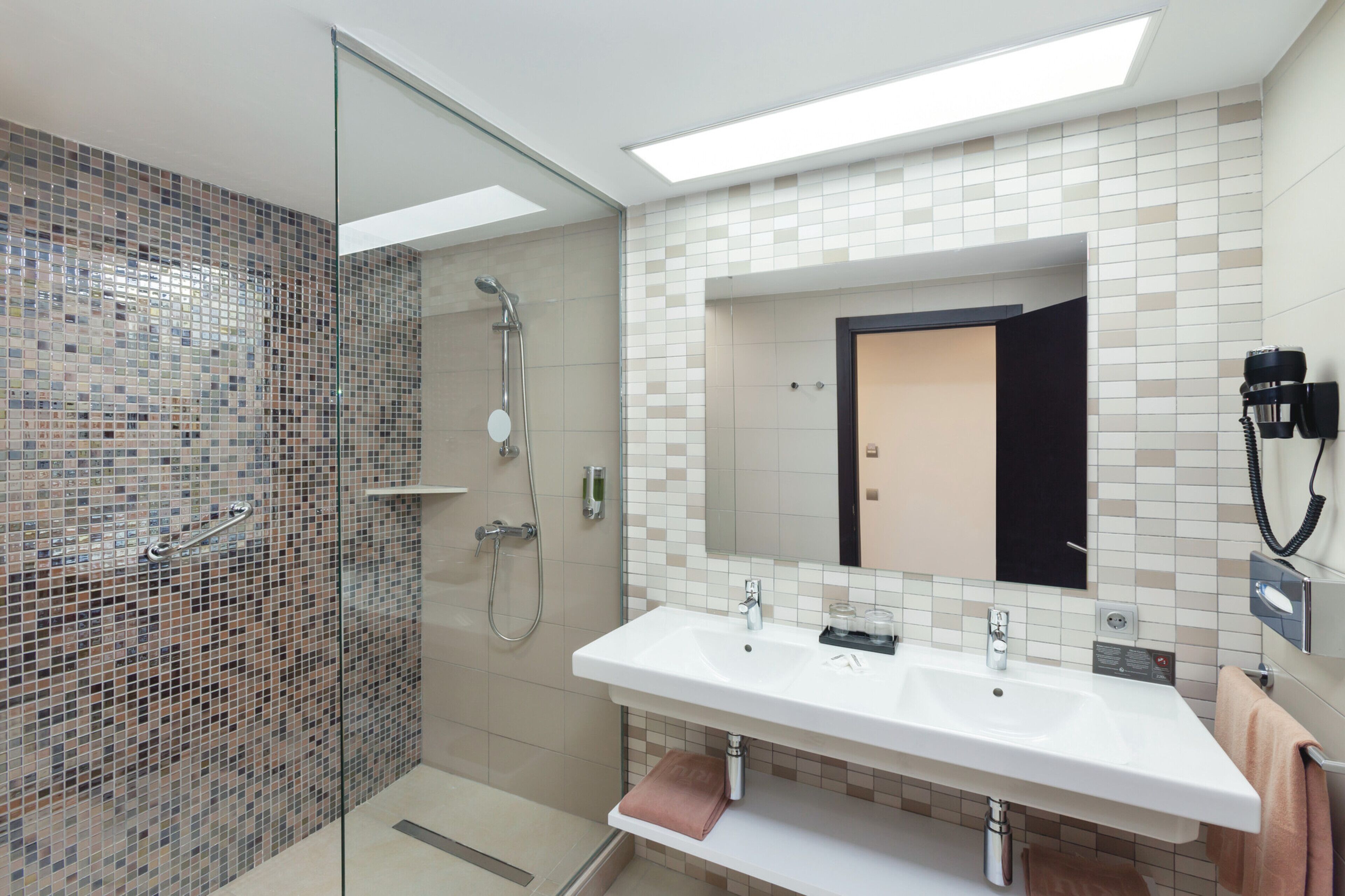 A modern bathroom with a glass-enclosed shower, a white sink with two faucets, and a large mirror above the sink.