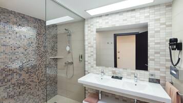 A modern bathroom with a glass-enclosed shower, a white sink with two faucets, and a large mirror above the sink.