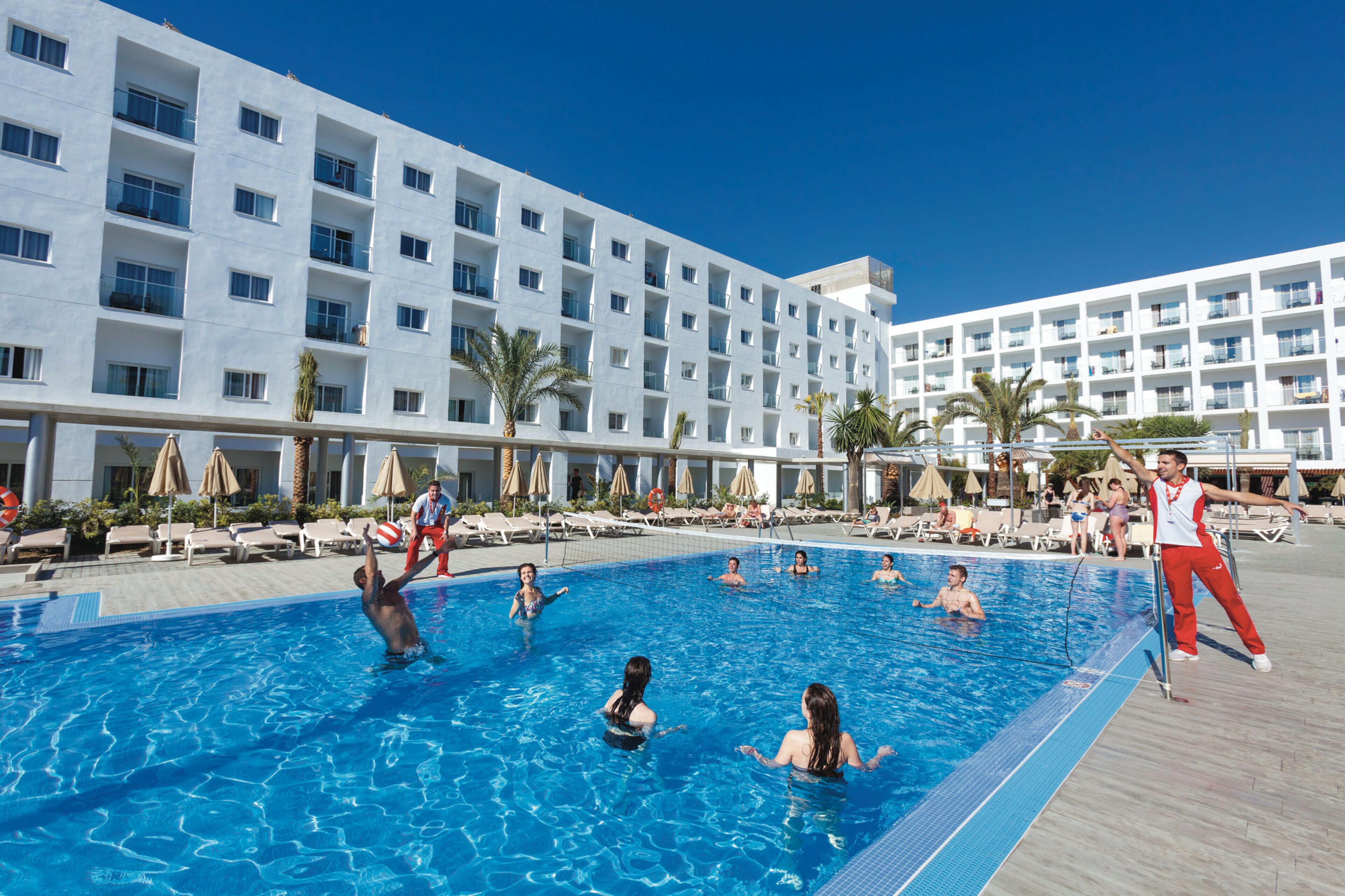 A swimming pool area with multiple levels of balconies, sun loungers, and palm trees.