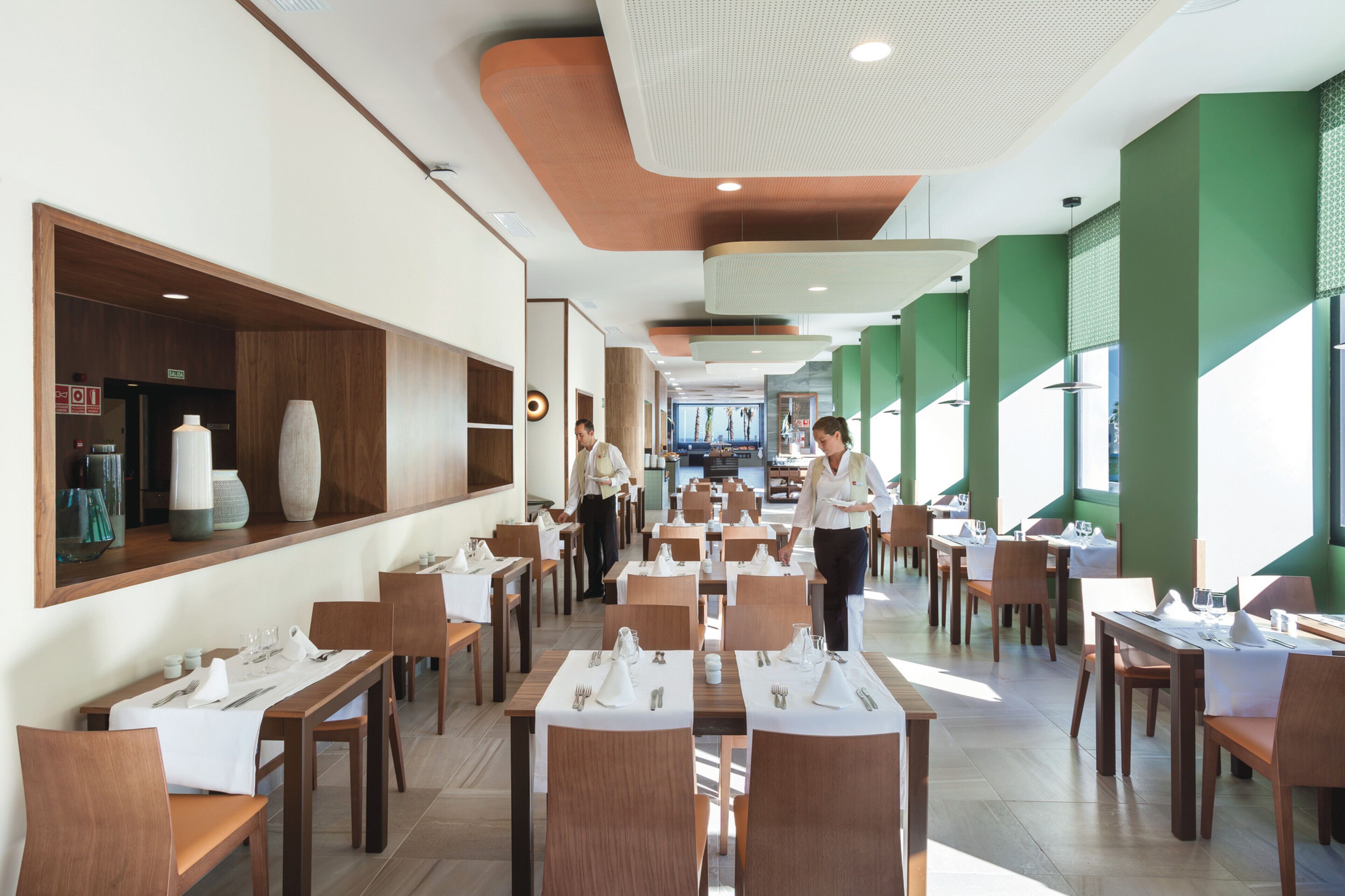 Un vaste espace dédié à la salle à manger, avec de nombreuses tables et chaises, un long comptoir agrémenté d’objets décoratifs et un design de plafond moderne.