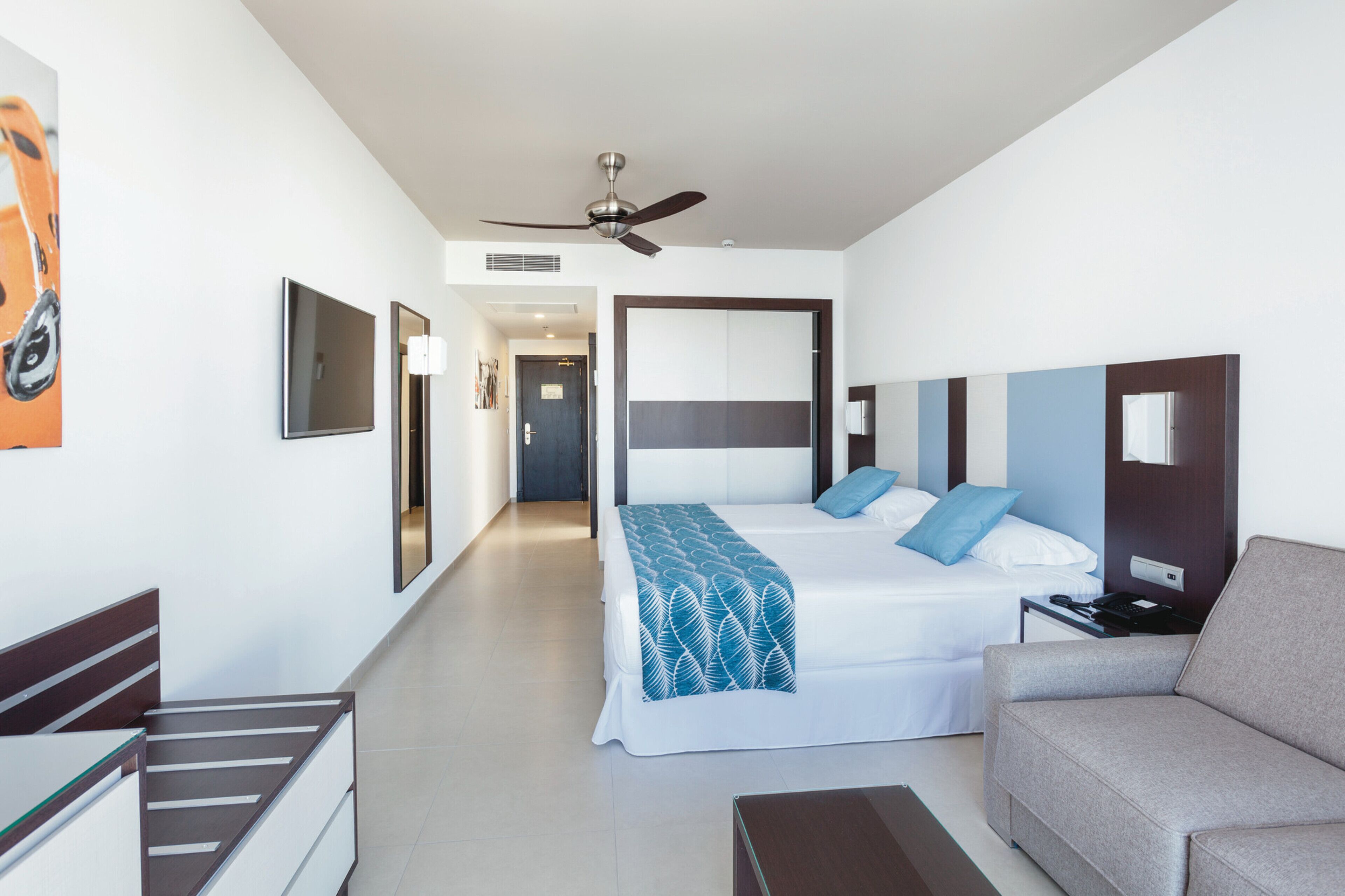 Een moderne hotelkamer met een bed, een slaapbank, een televisie en een plafondventilator.