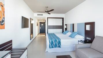 A modern hotel room with a bed, a sofa, a TV, and a ceiling fan.