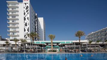 A hotel with a swimming pool, multiple balconies, and palm trees.