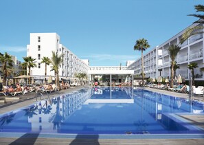 A swimming pool with lounge chairs and umbrellas, surrounded by palm trees and modern buildings.