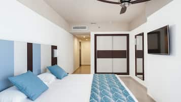 Habitación de hotel con cama, ventilador de techo, televisor y puerta que da a un pasillo.