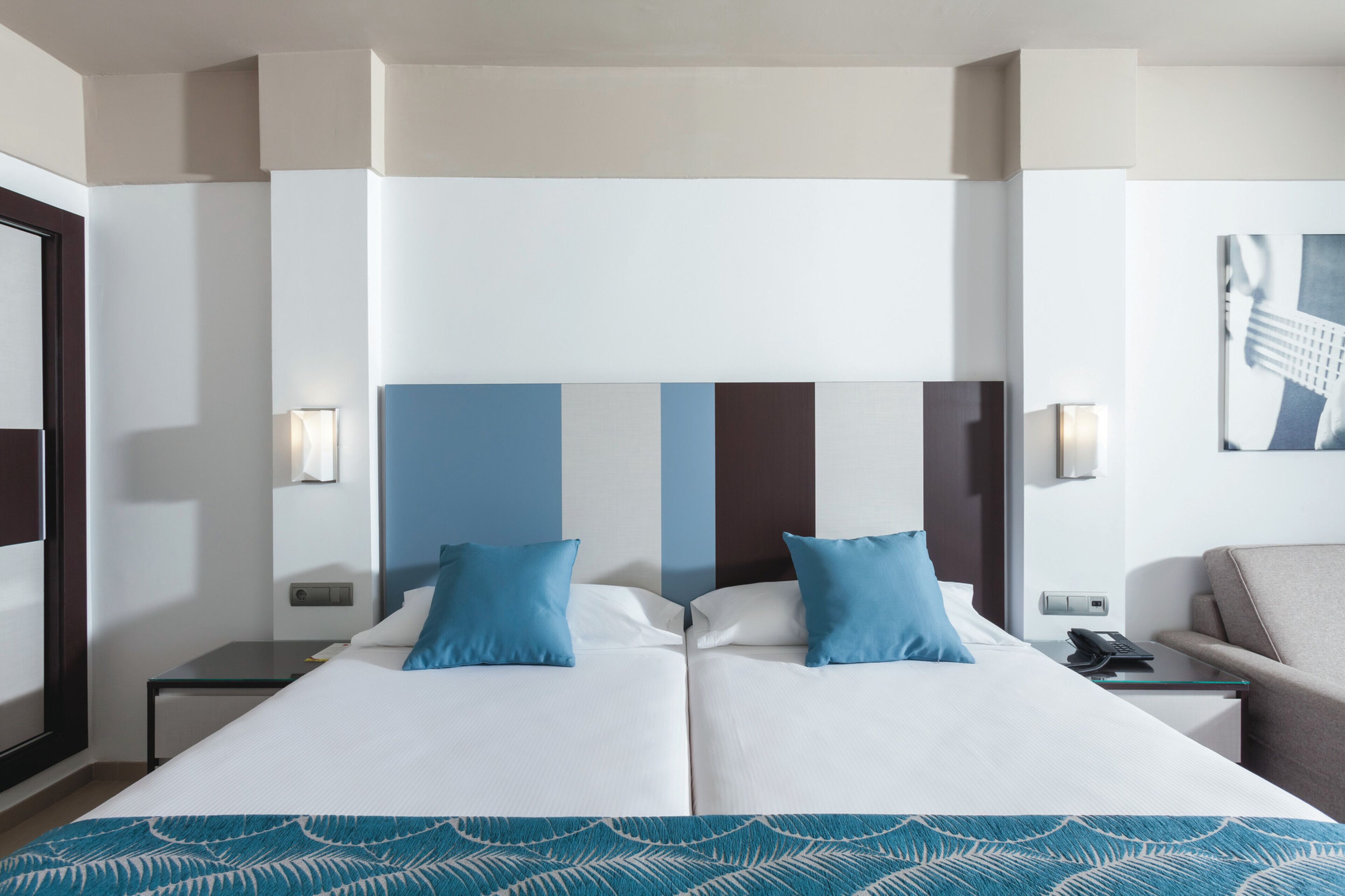 Une chambre d’hôtel avec un grand lit, deux oreillers, une table de chevet, une lampe et une chaise.