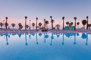 A poolside area with lounge chairs and palm trees, reflecting in the water. - Hotel Riu Costa del Sol - All Inclusive (Torremolinos)