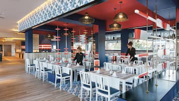 Een modern restaurant met wit en rood decor, meerdere eettafels en hangende吊灯.