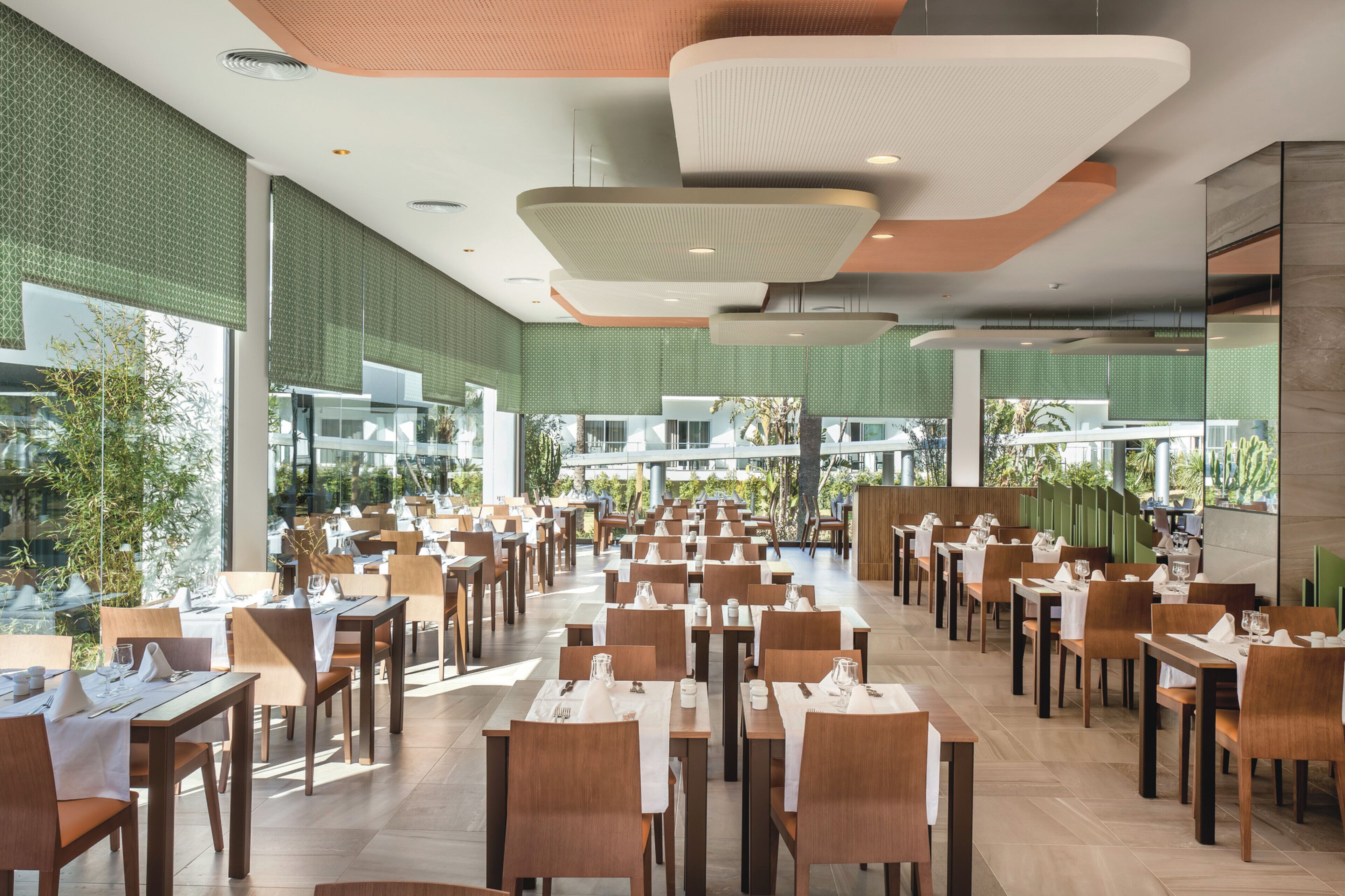 Un comedor espacioso con varias mesas y sillas, ventanas amplias y un diseño moderno en el techo.