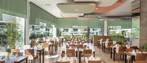 A spacious dining area with multiple tables and chairs, large windows, and a modern ceiling design.