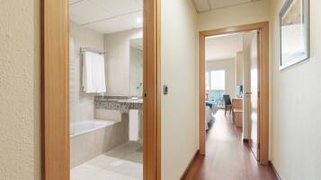 A hotel hallway with a bathroom featuring a bathtub, a sink, and a towel rack.