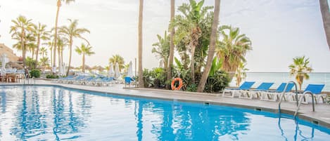 A swimming pool with clear blue water, surrounded by palm trees and lounge chairs.