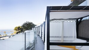 Un balcon avec un lit, une rambarde en verre et une vue sur la mer.
