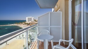Un balcon doté d’une balustrade en verre, offrant une vue sur une plage et l’océan, et comprenant une petite table et deux chaises.