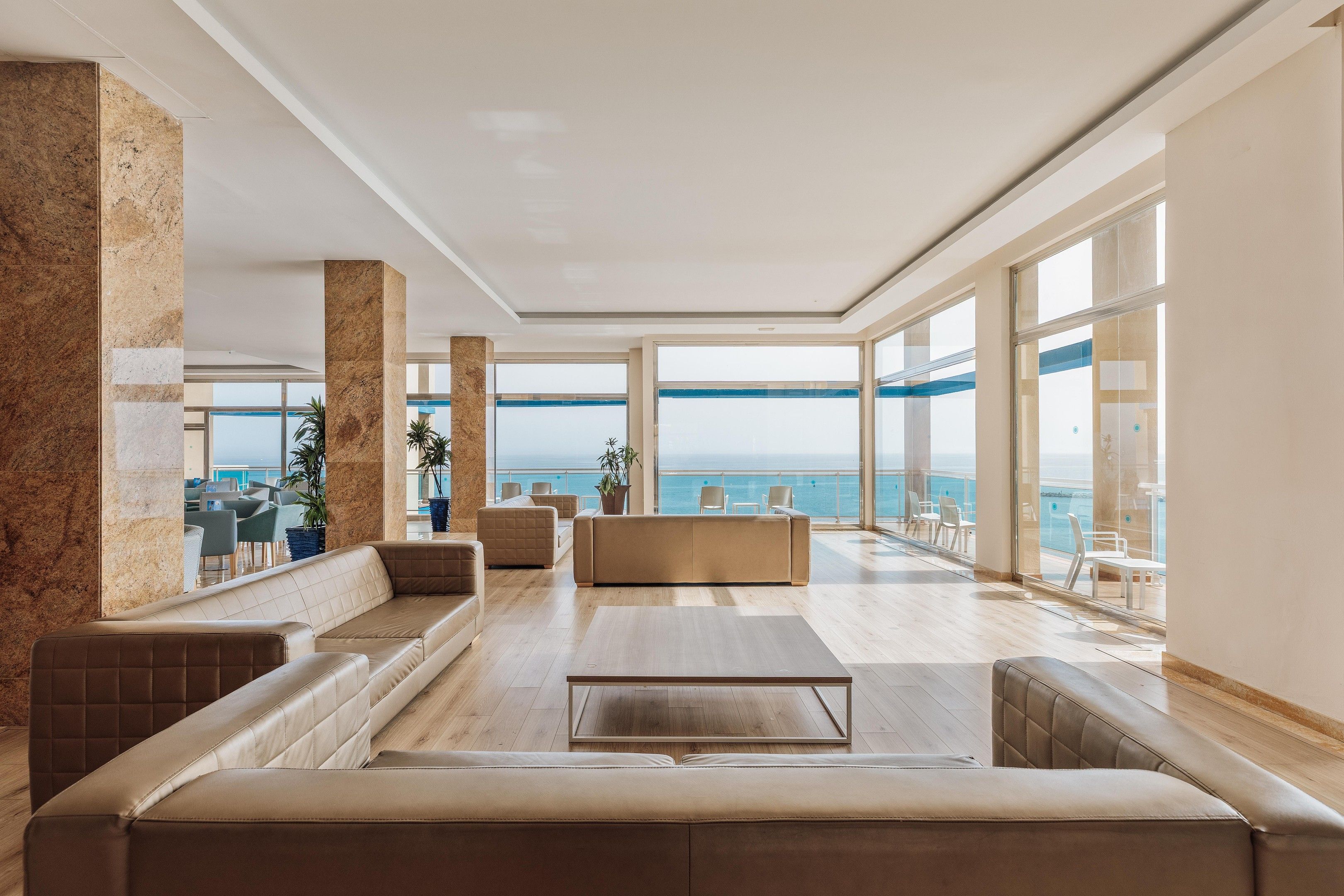 A spacious living area with a large window overlooking the sea, a seating area with sofas, and a view of the ocean.