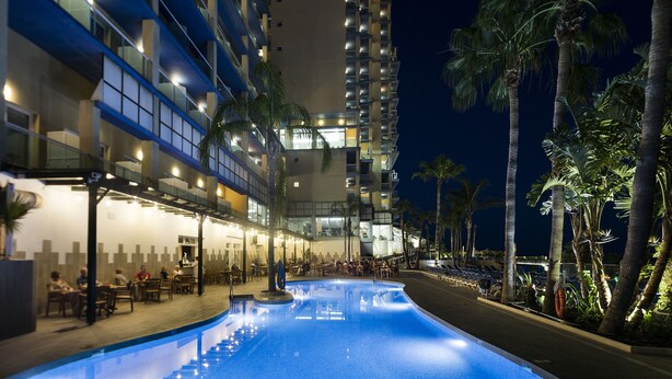 Un hôtel doté d’une piscine, d’un espace extérieur aménagé et de palmiers.