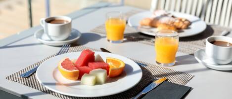 A breakfast table with a plate of fruit, two glasses of orange juice, and a cup of coffee.