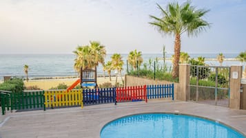 Piscina con vista al mar, rodeada de palmeras y una valla colorida.