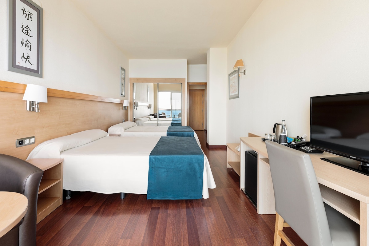 Une chambre d’hôtel avec deux lits, un bureau avec une télévision et une vue sur la mer.