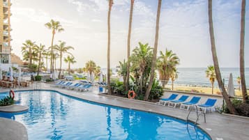 A swimming pool with lounge chairs and palm trees, overlooking a beach.