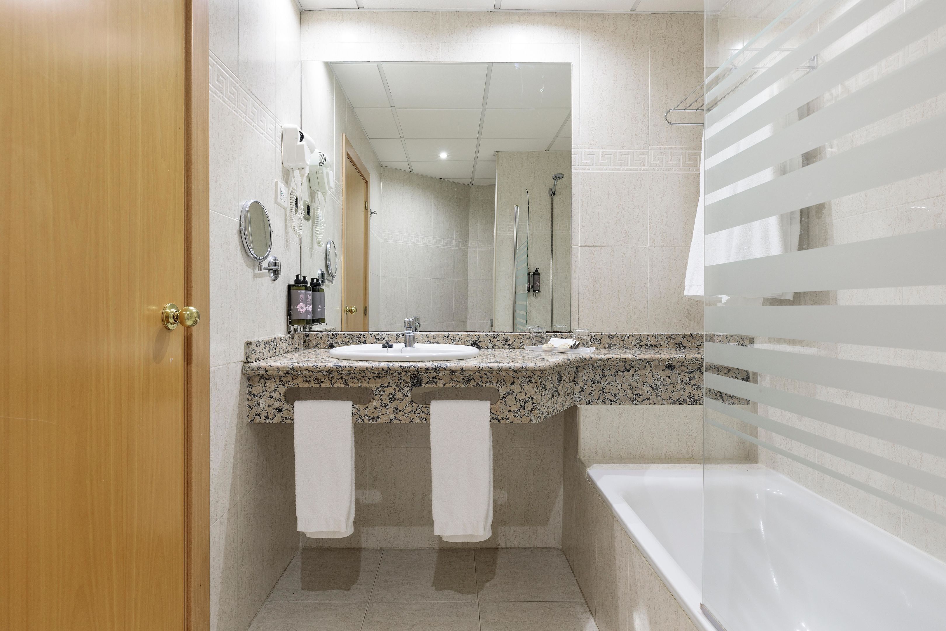 Uma casa de banho moderna com porta de madeira, uma pia com dois espelhos, chuveiro e banheira.