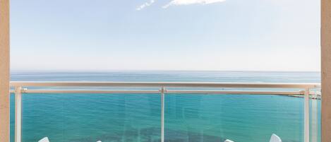 A balcony with a clear view of the ocean, two white chairs, and a small table.