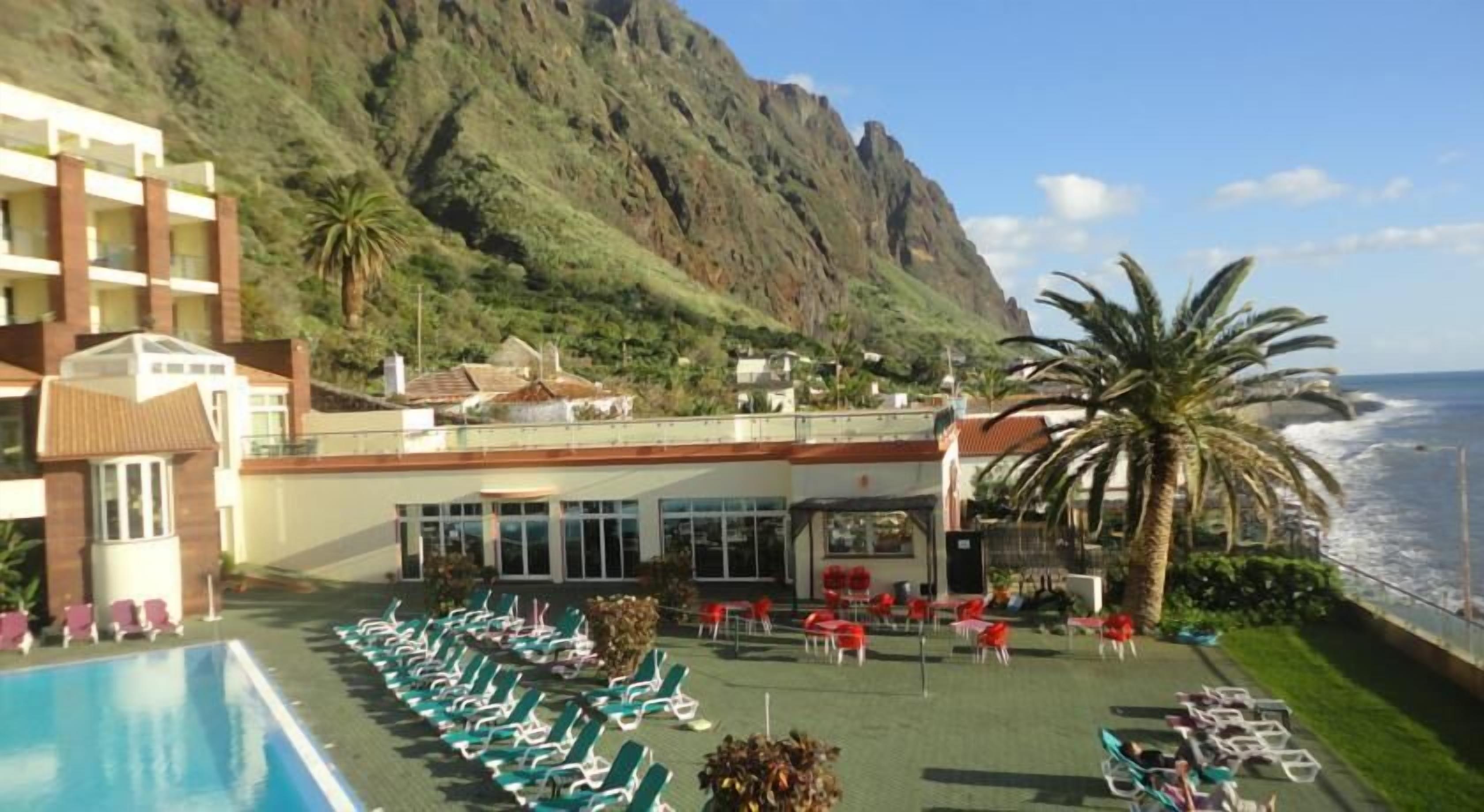 A hotel with a pool, sun loungers, and a view of the ocean.