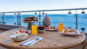 Une table à manger avec divers aliments pour le petit-déjeuner et un verre de jus d’orange, donnant sur une étendue d’eau.