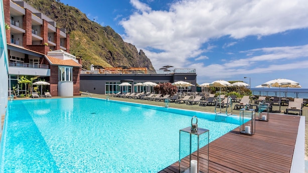 Un espace piscine avec des chaises longues et des parasols, une terrasse en bois et une vue imprenable sur les montagnes.