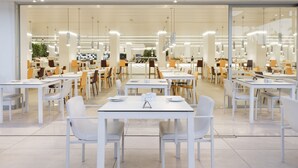 A modern dining area with white tables and chairs, overhead lighting, and a large glass wall. - Hotel Caserío (San Bartolomé de Tirajana)